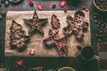 Homemade Christmas chocolate bars making. Christmas cutters with various toppings and flavorings filled with melted chocolate and caramel on dark rustic kitchen table background, top view