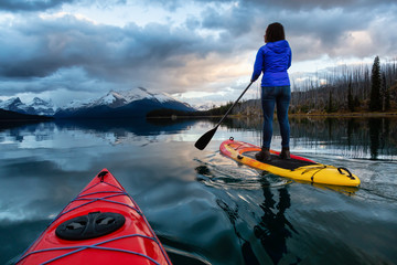Kayaking in a peaceful and calm glacier lake during a vibrant cloudy sunset. Taken in Maligne Lake,...