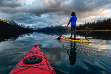 Kayaking in a peaceful and calm glacier lake during a vibrant cloudy sunset. Taken in Maligne Lake,...