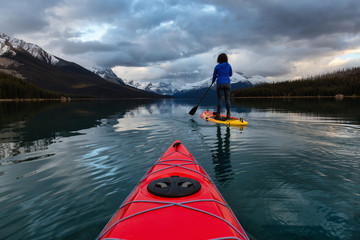 Kayaking in a peaceful and calm glacier lake during a vibrant cloudy sunset. Taken in Maligne Lake, Jasper National Park, Alberta, Canada.