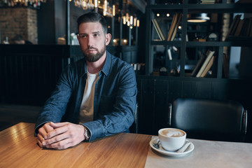 Confident man enjoying a cup of coffee while having work break lunch in indoors cafe looking pensive