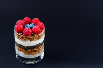 Healthy blueberry and raspberry parfait in a glass on a black background. Two portions. Space for text or design.