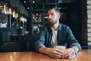 Confident man enjoying a cup of coffee while having work break lunch in indoors cafe looking pensive