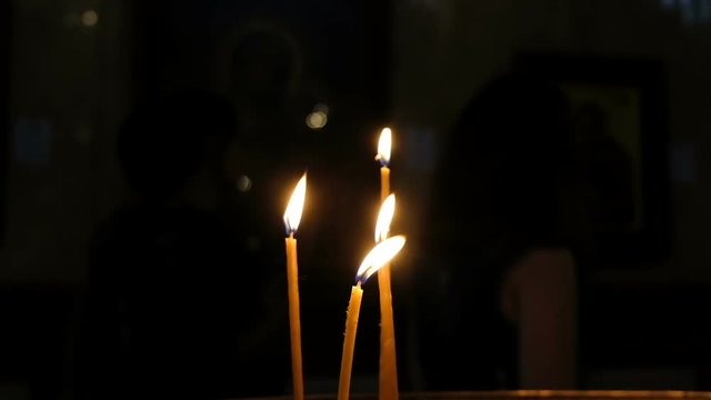 Four candles burning in the church in the dark against the background of people, slow motion