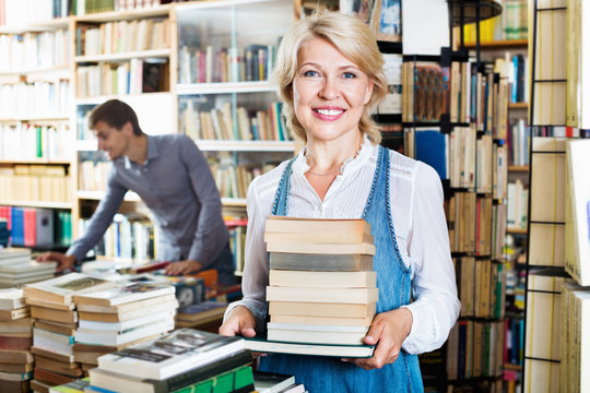 Smiling mature woman holding book pile