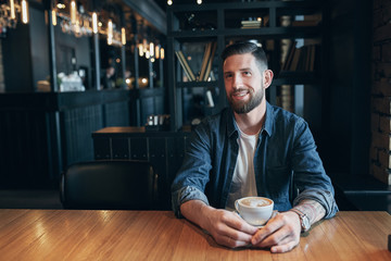 Confident man enjoying a cup of coffee while having work break lunch in indoors cafe looking pensive