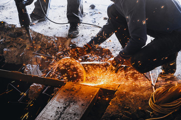 Male worker saws a disk grinding saw armature into a reinforced concrete panel, the destruction of the old house. Sparks from friction with metal. Rescue work.