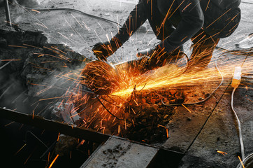 Male worker saws a disk grinding saw armature into a reinforced concrete panel, the destruction of the old house. Sparks from friction with metal. Rescue work. - obrazy, fototapety, plakaty
