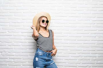 Portrait of woman posing trendy straw hat and sunglasses against white brick wall.