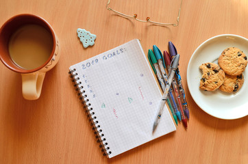 2019 New year's goals on a notebook on a wooden table with glasses, cookies, cup of coffe, a blue Christmas tree and pens