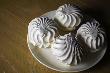Marshmallow four delicious sweet desserts of white marshmallows zephyr on a plate in contrast lighting on a wooden table. Lack of coverage. Evening