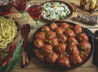 Homemade meatballs in tomato sauce. Frying pan on a wooden surface, rice with vegetables, pasta