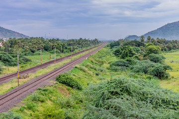 straight railway track goes to horizon in green landscape under blue sky with clouds.