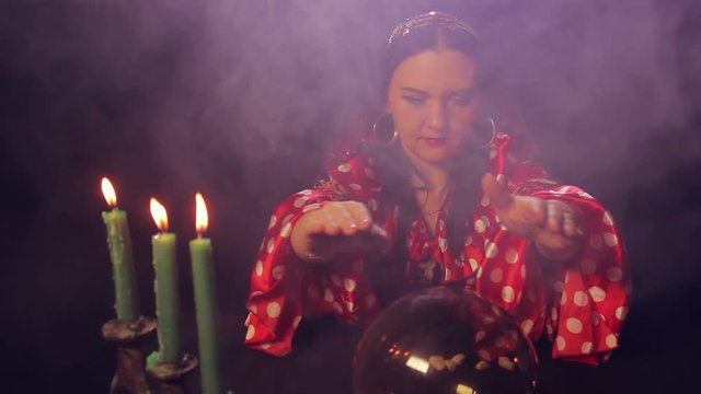 A gypsy fortune teller at the table reads the future in a magic ball.