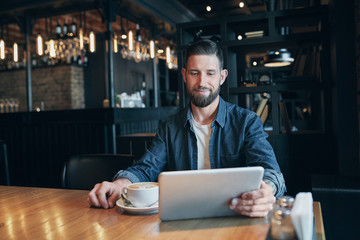 Young man drinking coffee in cafe and using tablet computer