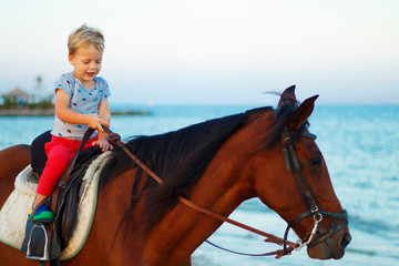 Obraz premium Cute little boy rides a horse on the beach. Copy space