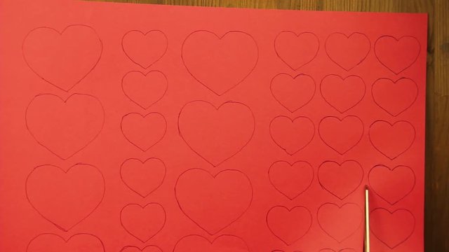 The girl cuts blanks of hearts from red cardboard. Close-up