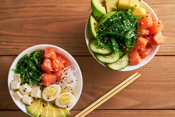 Raw Organic Poke Bowl with with rice, avocado, salmon, mango, cucumbers, chuka salad, quail eggs,...