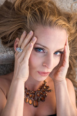 Obraz premium Closeup portrait of a beautiful woman lying and posing on the stairs and wearing a necklace on a sunny day.