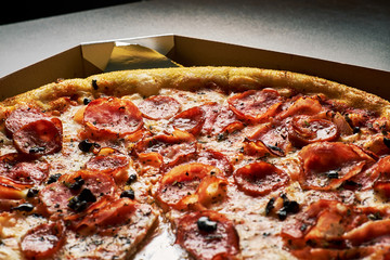 Pizza with bacon in a cardboard box on a dark background. Close-up. View from above. Pizza delivery. Pizza menu.