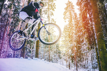 Naklejka premium Silhouette of a cyclist in a jump. Mountain biking on trails in a snowy forest. Extreme winter sport. Bike rider flies through the air