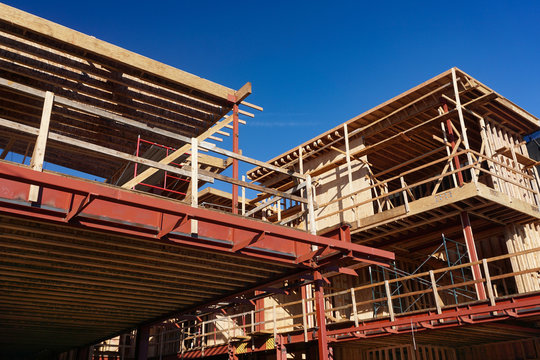 Residential apartment or condo construction site in southern California with steel beams and girders, wood carpentry framework, scaffolding and cross braces under a bright blue sky 