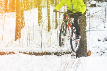 Silhouette of a cyclist in a jump. Mountain biking on trails in a snowy forest. Extreme winter sport. Bike rider flies through the air