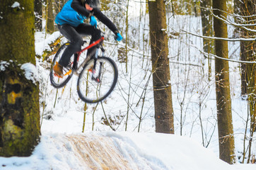 Naklejka premium Silhouette of a cyclist in a jump. Mountain biking on trails in a snowy forest. Extreme winter sport. Bike rider flies through the air