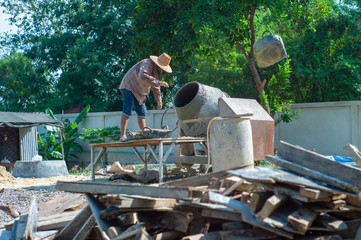 Worker throws away the rubber container of mixing material while using the concrete mixer at the construction site