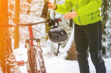 Male racer hangs helmet and gloves on the handlebars of a bicycle in snowy winter forest.. Break training for rest. Extreme sport background. Mountain bike safety concept.