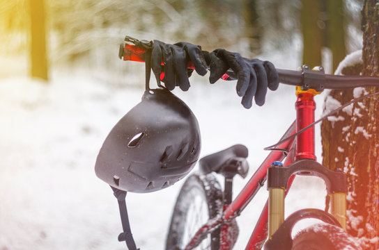 Black helmet with black sport gloves hangs on the handlebars of a bicycle in snowy winter forest. Mountain bike safety concept. Extreme sport background