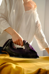 Girl ironing clothes  at home a yellow jacket