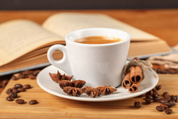 Coffee break a Cup of hot coffee and a book on a wooden table. A white Cup of black coffee surrounded by a small amount of roasted coffee beans, cinnamon, anise and an open book