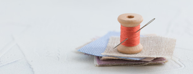 Coral colored threads wooden bobbin for stitching with a needle on a white background, banner