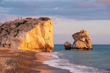 Beautiful afternoon view of the beach around Petra tou Romiou, also known as Aphrodite's birthplace, in Paphos, Cyprus. People climb the rock in the distance.