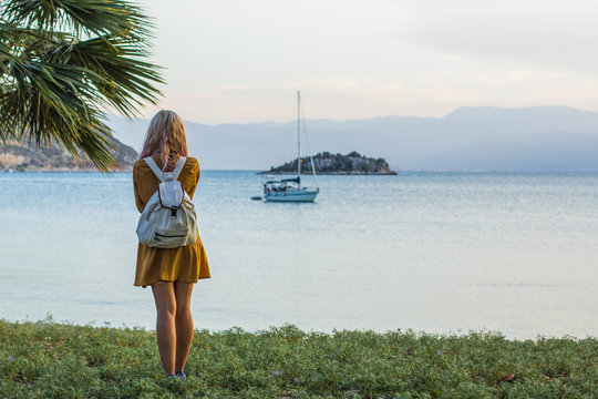 travel adult backpack girl stain back to camera under park and taking photo of beautiful tropic sea bay landscape with yacht on calm water surface and island in soft evening colors before sunset