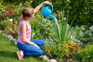 Caucasian young woman watering flowers with water can at a household plot. Side view. © Artem