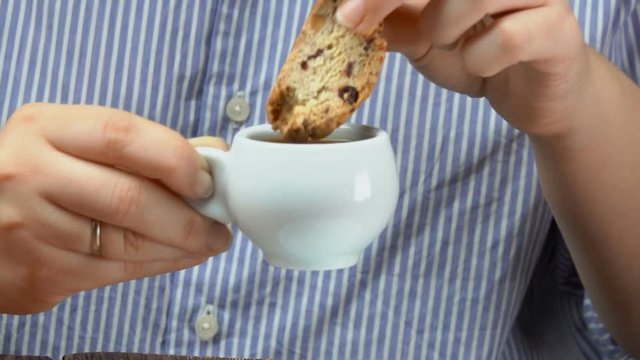 Hand dunks italian biscotti with almond and cranberries into an espresso cup