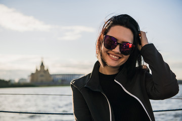 Beautiful female enjoying her free time by the river. Girl Outdoor Lifestyle. Young woman with black hair wearing sunglasses.