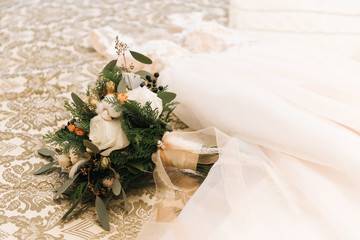 Winter bride's bouquet with roses, cotton, spruce lies next to the wedding dress in a luxurious hotel room © ksyusha_yanovich
