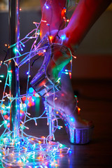 Fototapeta na wymiar Strip-shoes with female legs dancing on a pole silver shoes wrapped by bunch of Christmas lights