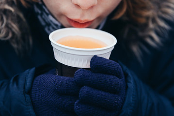 Close-up of popular hot non-alcoholic beverage, called Punsch in German language. Children hands in blue winter gloves holding a cup with favourite hot drink on Christmas markets in Switzerland and in