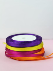 A stack of satin color rolls of bright blue, purple, yellow and green ribbons on a pink background for decoration and gift wrapping vertical