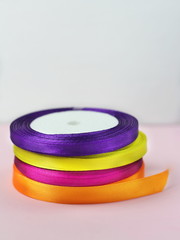 A stack of satin color rolls of bright blue, purple, yellow and green ribbons on a pink background for decoration and gift wrapping vertical
