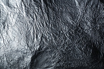 Thin wrinkled sheet of crushed tin aluminum silver foil background texture 