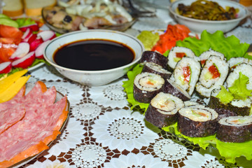 Sushi lay on the green leaves next to the soy sauce.