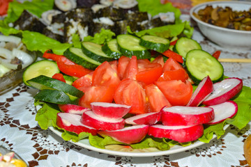 Tomatoes, cucumbers, radishes, sliced lie on a dish, dressed with olive oil for vegetarian food on a festive table.