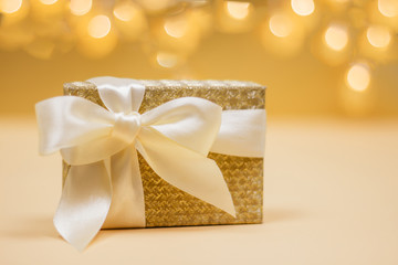 Golden present box with a bow on the bokeh lights background.