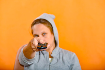 The girl the girl in the hood looks at the remote and switches the channels on TV.