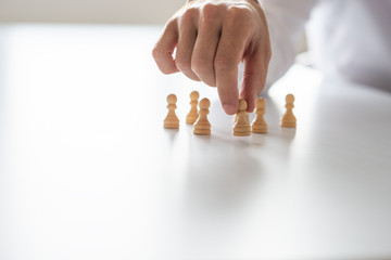 Closeup of businessman hand arranging peasant chess pieces on white office desk